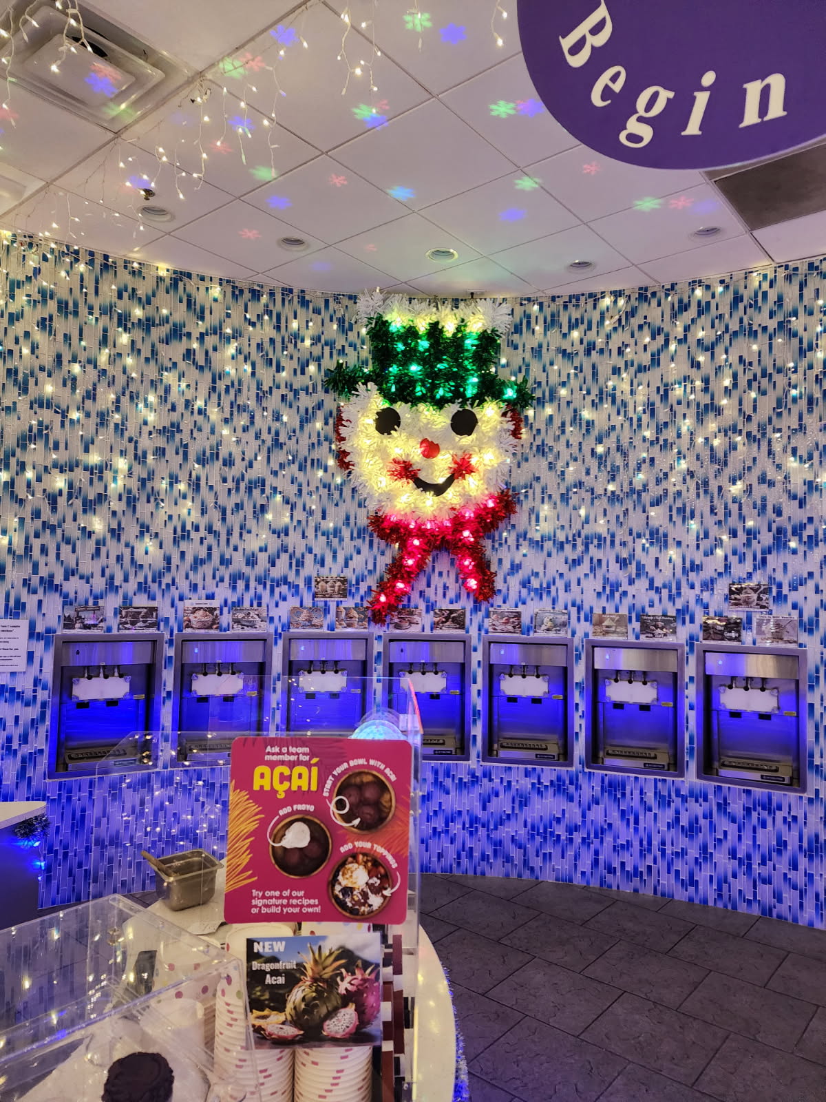 Frosty Froyo interior featuring frozen yogurt machines, festive illuminated snowman decoration, and colorful blue mosaic tile walls in Champions Gate